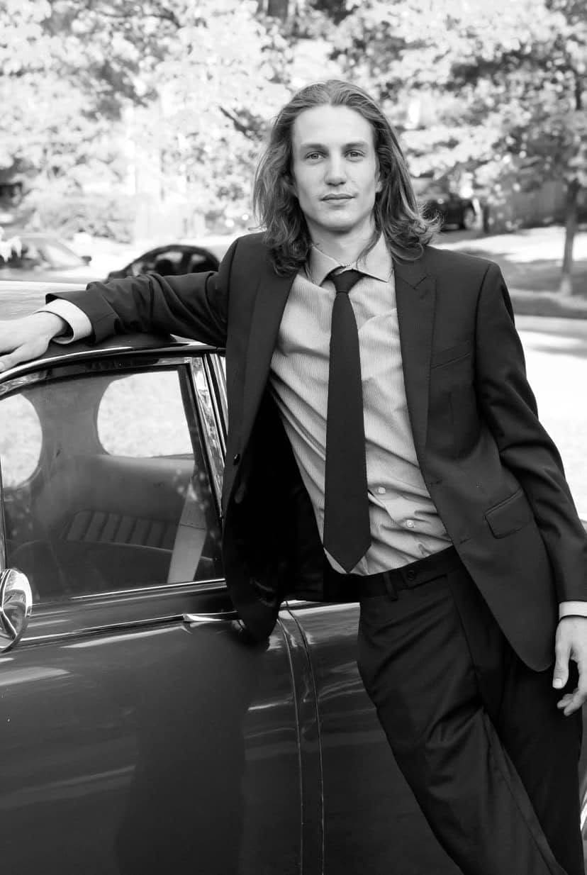 Black and white actor portrait leaning against a car